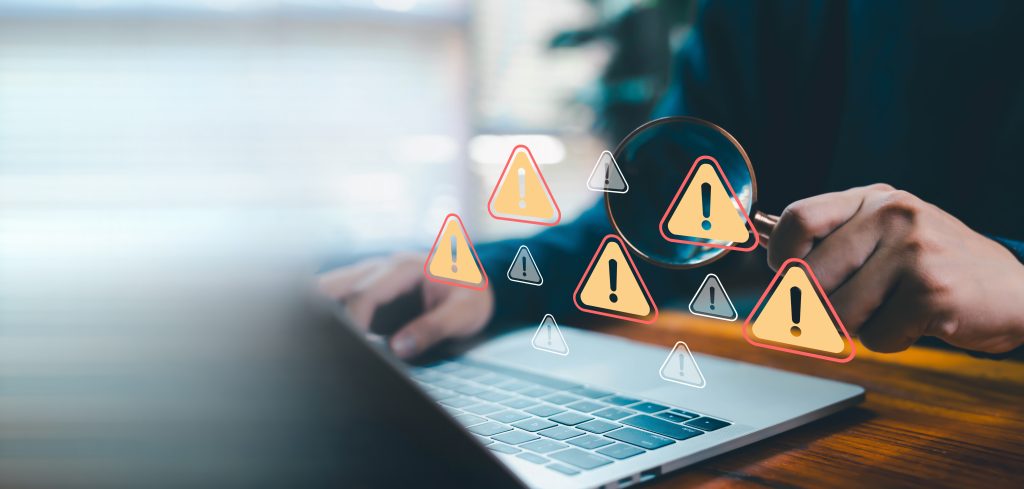 Magnifying glass highlighting multiple warning symbols over a laptop screen, representing scrutiny of inaccurate provider data and ghost network risks.